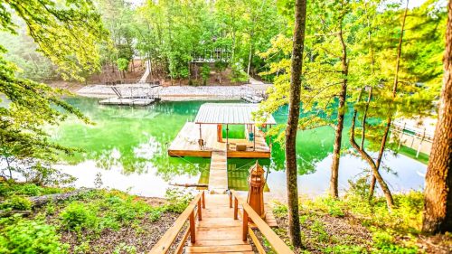 A wooden dock extends into a serene green lake, surrounded by lush trees and a peaceful natural setting.