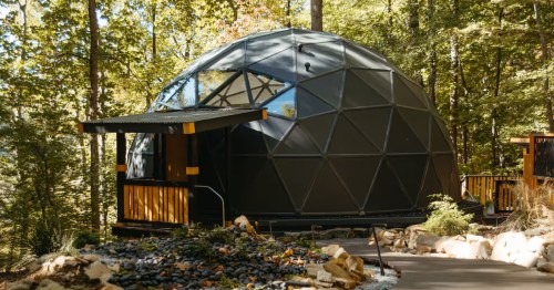 Exterior view of a modern glamping dome nestled in a lush Georgia forest with a large panoramic window reflecting the surrounding trees.