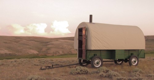 A covered wagon Airbnb in Shirley Basin, Wyoming, sits in an empty prairie at dusk.