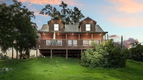 A charming wooden house with a deck, surrounded by greenery, under a colorful sunset sky.
