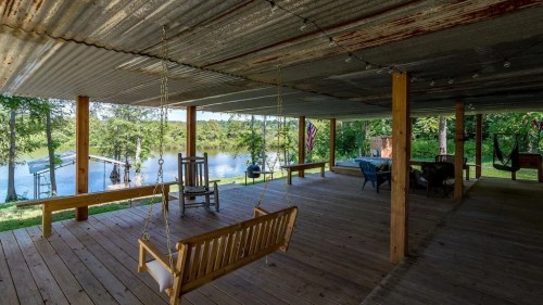 A rustic porch with wooden swings and seating, overlooking a serene pond surrounded by greenery.