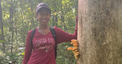 Host Lateefah standing by a tree with a mushroom growing on it on forage in Aurora, Illinois.