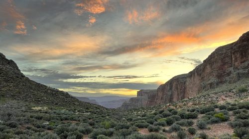 A scenic view of a canyon at sunset, with colorful clouds and lush greenery in the foreground.