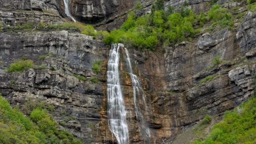 A stunning waterfall cascading down rocky cliffs, surrounded by lush green trees and rugged terrain.