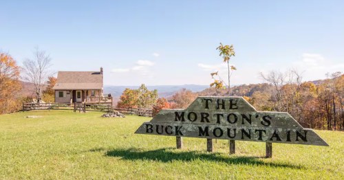 A rustic wooden sign reading 'The Morton's Buck Mountain' in front of a quaint cabin with a view in Virginia.