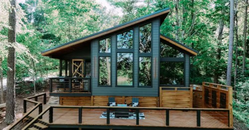 Modern cabin surrounded by green trees with a slanted roof and large windows