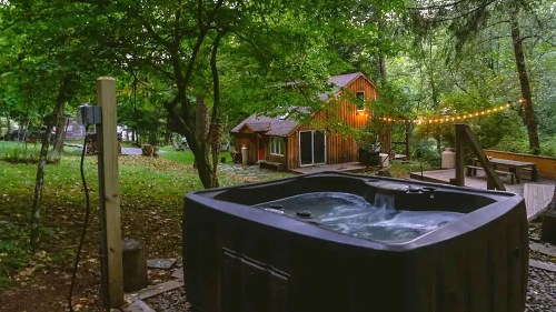 A hot tub surrounded by trees and a cozy cabin, with string lights illuminating the serene outdoor setting.