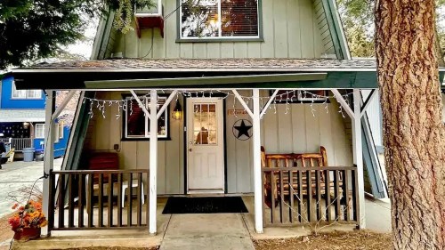 A cozy A-frame cabin with a porch, surrounded by trees and holiday lights, inviting and charming.