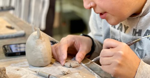 Artist using a detailing tool to sculpt a small clay figure during a pottery workshop.