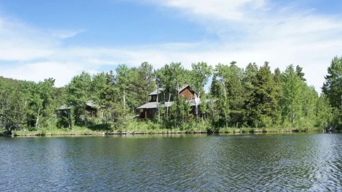 A serene lake scene with a house surrounded by trees under a clear blue sky.