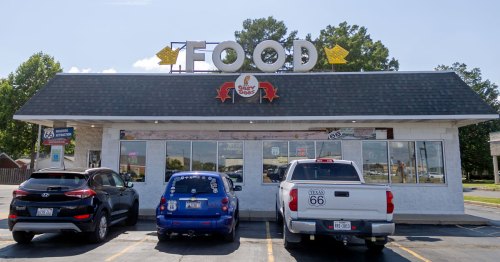 A "food" sign stands on top of a white building with cars in the foreground.