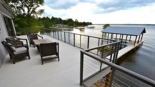 A lakeside deck with seating and a view of a dock and water under a cloudy sky.