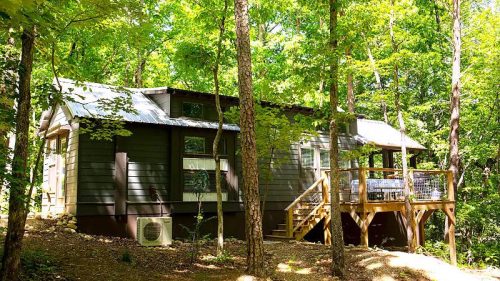 A cozy cabin nestled among trees, featuring a wooden deck and surrounded by lush greenery.