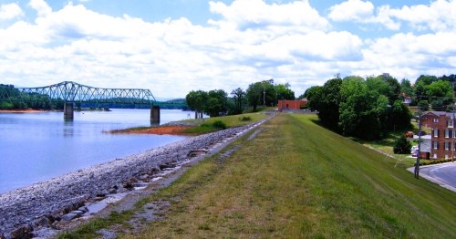 Dandridge, Tennessee with waterfront views, featuring a green bridge in the distance, framed by lush trees and a grassy embankment.
