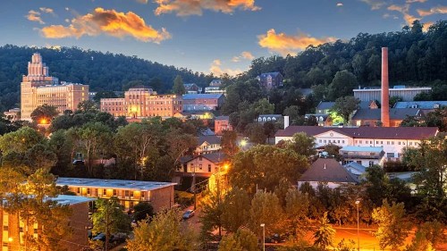 A scenic view of a town at dusk, featuring buildings, trees, and a colorful sky with clouds.