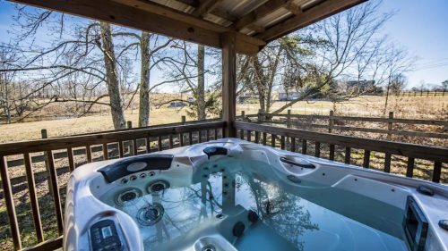 A hot tub on a wooden deck, surrounded by trees and a scenic view of a field.