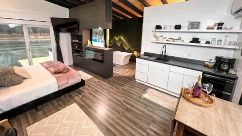 Cozy modern cabin interior with a bed, kitchenette, and large windows overlooking a serene outdoor view.