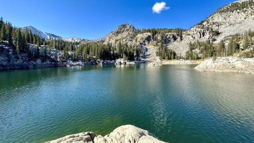 A serene lake surrounded by rocky mountains and lush green trees under a clear blue sky.