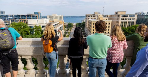 A group admires a lake and buildings from a rooftop.