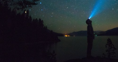Silhouette of a man using a headlamp to view a starry night sky over water at Ozark National Scenic Riverways.
