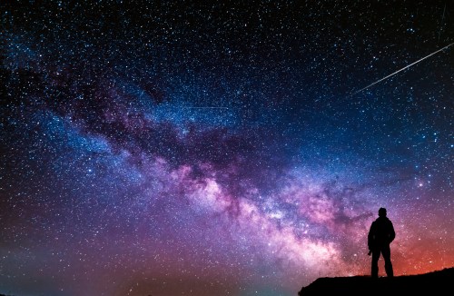 The Milky Way dances in front of the silhouette of a man.