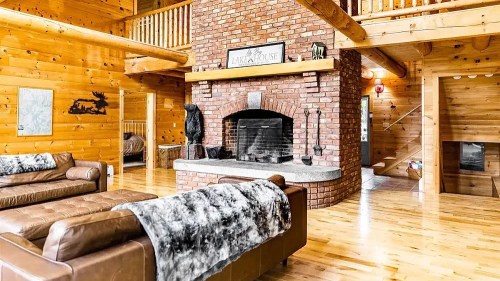Cozy log cabin interior featuring a brick fireplace, wooden beams, and comfortable leather sofas. Warm and inviting atmosphere.