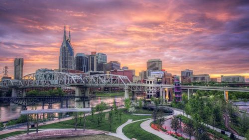 Sunset over Nashville skyline with vibrant clouds, bridges, and green parks along the riverbank.