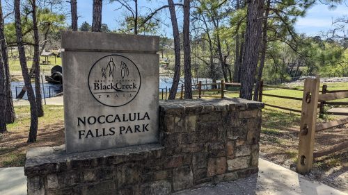 Sign for Noccalula Falls Park at Black Creek, surrounded by trees and a scenic landscape.