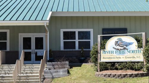 Exterior of River Park North building in Greenville, NC, featuring a green roof and a sign with a bluebird logo.