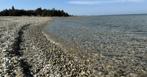 Crystal clear water ripples over a rocky pebble beach along the coast of Wilderness State Park, Michigan.