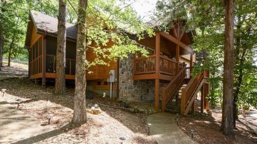 A cozy wooden cabin surrounded by trees, featuring a stone facade and a welcoming porch with steps.
