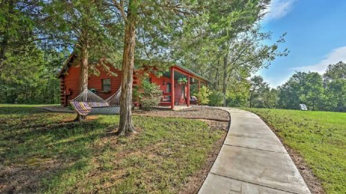 A cozy log cabin surrounded by trees, with a hammock and a winding path leading to the entrance.