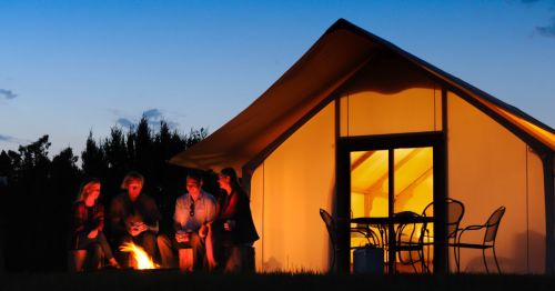 Group of people sitting around a campfire in front of a glowing glamping tent at Royal Gorge Cabins in Cañon City, Colorado.