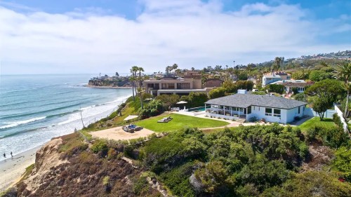 Aerial view of a coastal property with a lawn, overlooking the ocean and nearby homes along the shoreline.