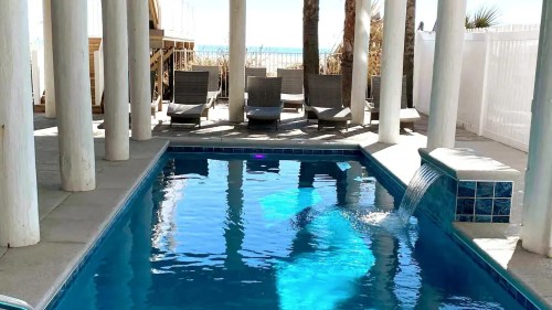 A serene pool area with lounge chairs, surrounded by palm trees and a view of the beach in the background.