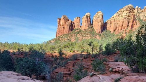 Rocky landscape with two water pools in the foreground and towering red rock formations in the background under a clear blue sky.