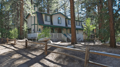A large, two-story house surrounded by tall trees and a wooden fence in a forested area.