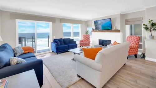 Bright living room with ocean view, featuring blue and orange sofas, a TV, and a cozy atmosphere.