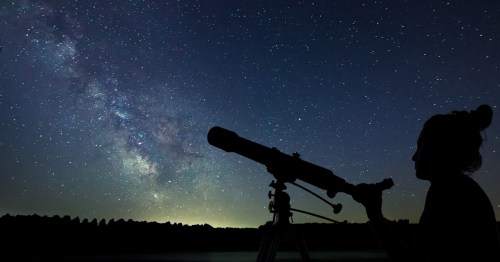 A woman with a telescope looks up at the Milky Way.