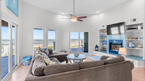 Cozy living room with a large sectional sofa, ceiling fan, and ocean view through sliding glass doors.