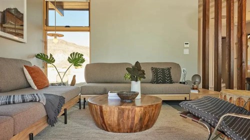 Modern living room with gray sofas, a wooden coffee table, plants, and natural light from large windows.