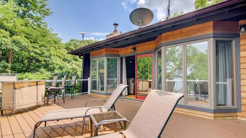A wooden deck with lounge chairs, a dining area, and large windows overlooking a lush green landscape.