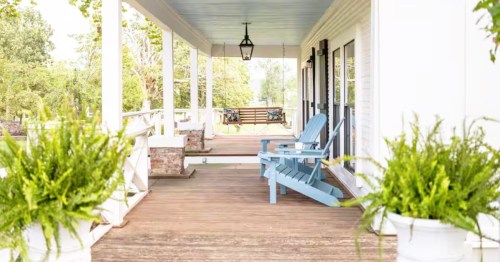 A porch featuring light blue Adirondack chairs, potted ferns, and a swing, at a charming 100-year-old cottage Airbnb on Beaver Lake in Lowell, Arkansas.