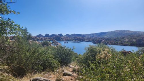 A serene lake surrounded by rocky hills and lush greenery under a clear blue sky.
