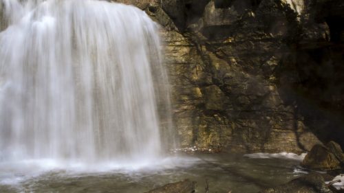 A serene waterfall cascading over rocky cliffs into a calm pool below, surrounded by nature.