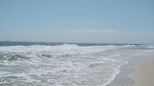 A serene beach scene with gentle waves lapping at the shore under a clear blue sky.