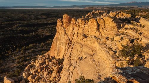 A rugged rock formation rises above a vast, green valley under a clear sky, showcasing natural beauty and geological features.