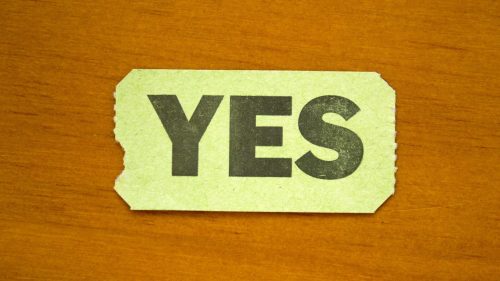 A green ticket with the word "YES" printed in bold black letters on a wooden surface.