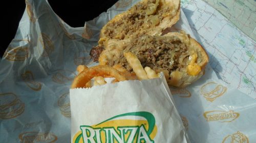 A Runza sandwich with meat and cheese, alongside a bag of curly fries, on a paper wrapper and a map in the background.