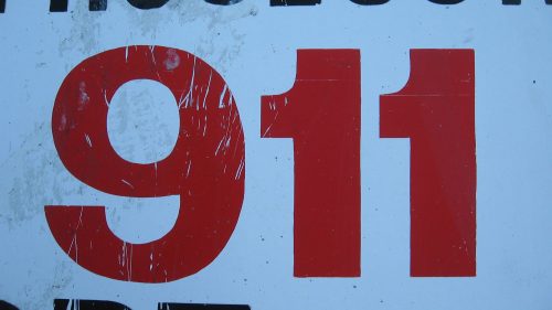 Red numbers "911" on a weathered white sign, with scratches and dirt visible on the surface.